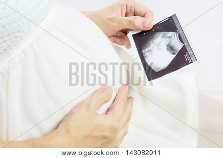 Pregnant asian woman looking at ultrasound scan of baby close up of scan