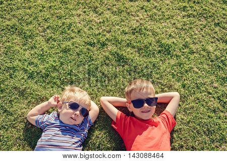 Happy smiling kids relaxing on green grass under sun top view with copy space. Color-toning applied