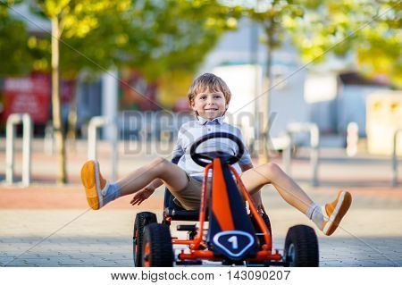 Active little kid boy driving pedal race car in summer garden, outdoors. child racing with fast speed and having fun.
