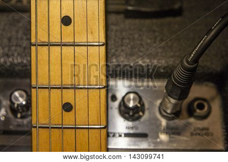 Guitar neck over amplifier device and audio cord with jack closeup