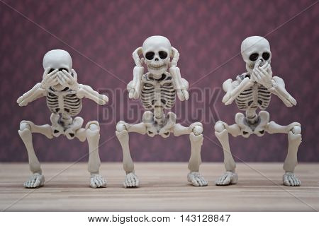Three skeletons pose as three wise monkey