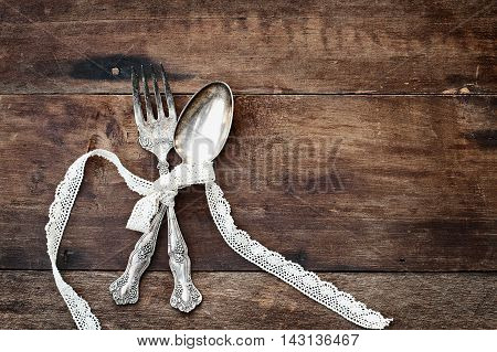Antique silverware spoon and fork tied with lace ribbon over a rustic old wooden background with a grunge like feel. Image shot from overhead.