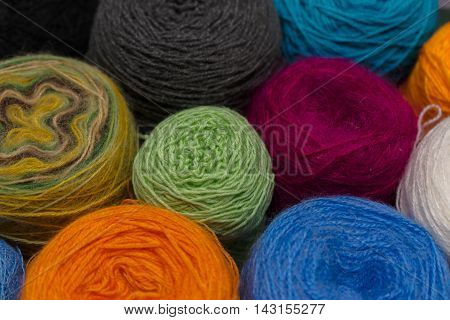 Many small balls of wool of rainbowcolors on the wooden table.