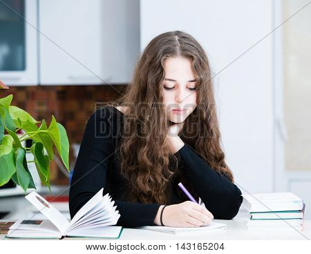 The young girl is studing in the kitchen