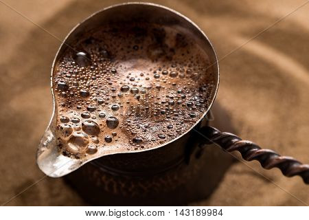 Coffee brewing in turkish pot in hot sand, cezve. Closeup shot, top view.