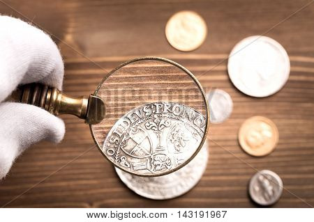 Examining antique silver coin through magnifying glass on wooden table