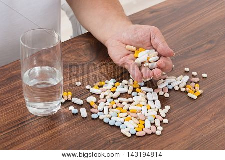 Close-up Of A Person's Hand Holding Pills With Glass Of Water On Desk