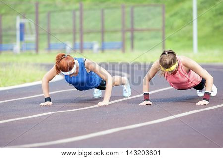 Sport Concepts and Ideas. Two Professional Female Athletes Doing Pressing Ups At Sport Venue Outdoors. Horizontal Image