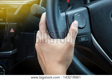 A woman hand pushes the volume control button on a steering wheel.