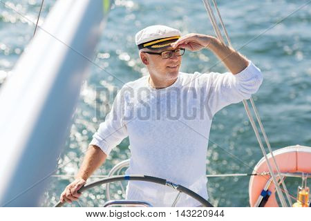 sailing, age, tourism, travel and people concept - happy senior man in captain hat on steering wheel and navigating sail boat or yacht floating in sea