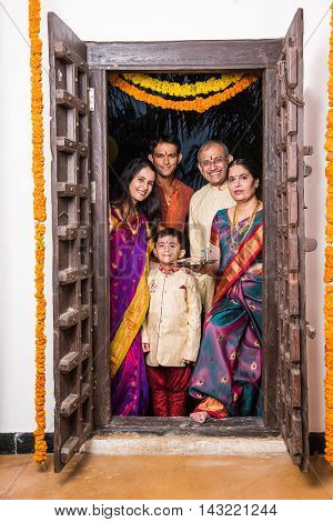 indian family group photo while entering house with puja thali at old antique door, gruha pravesh
