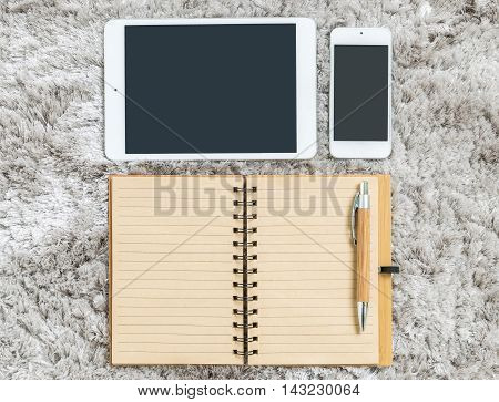 Closeup brown note book with line in page brown pen tablet and smart phone on gray fabric capet textured background in top view in work concept