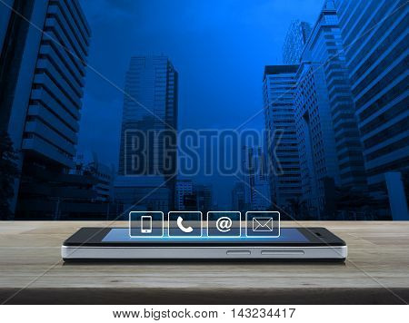 Telephone mobile phone at and email buttons on modern smart phone screen on wooden table over city tower background Customer support concept