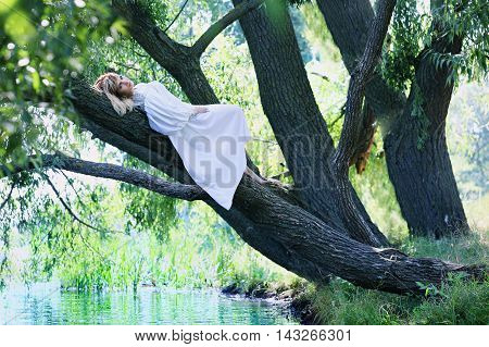 Beautiful woman in white dress lying on a tree over the river