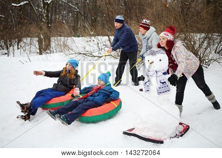 Three adults let go down from hill two children on snowtubes at winter