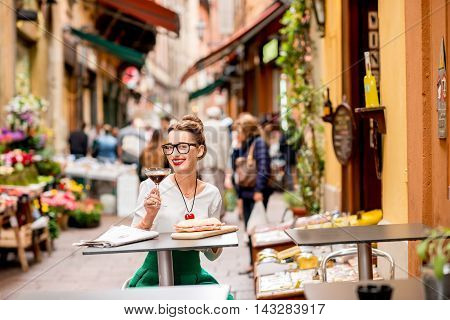 Young woman sitting at the cafe with shakerato coffee and panini outdoor on the famous street with local food markets in Bologna city.