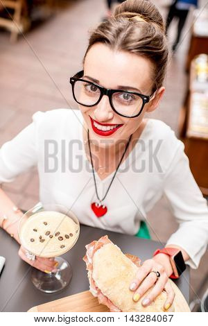 Young woman with shakerato coffee drink and panini with prosciutto outdoor.