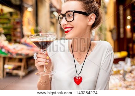 Young woman sitting at the cafe with shakerato drink in cocktail glass outdoor. Traditional italian cold coffee