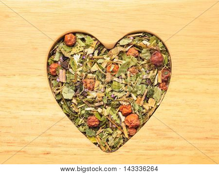 Dried herb leaves heart shaped on wooden surface. Herbaceous dry aromatic plant. Healing herbs herbal medicine concept.