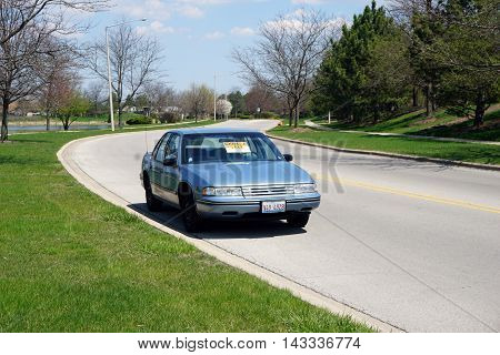 JOLIET, ILLINOIS / UNITED STATES - APRIL 19, 2016: A sign on the windshield of a blue automobile, parked on the Wesmere Country Club's Wesmere Parkway, indicates the direction of a garage sale.