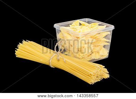 Uncooked bow-tie pasta in transparent plastic tray and bundle of dried long pasta on a dark background