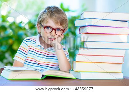 Frustrated and sad little kid boy with glasses and lots of colorful books. Child and student is back to school and is tired and disappointed on warm day.