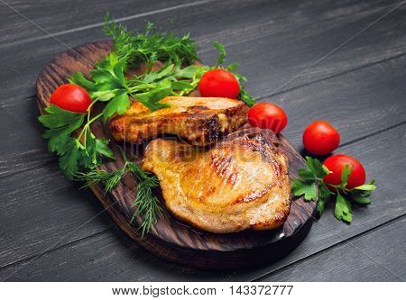Grilled meat pork chops served in grill board ingredients for meat pork chops dill parsley lettuce cherry tomatoes dark black wood background