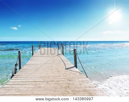 Boardwalk or gangplank into the sea. Wooden pier or jetty and turquoise, wavy sea with bright sun and copy space. Beach background.