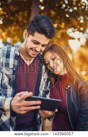 Young couple in the park during autumn season outdoor - using tablet technological device