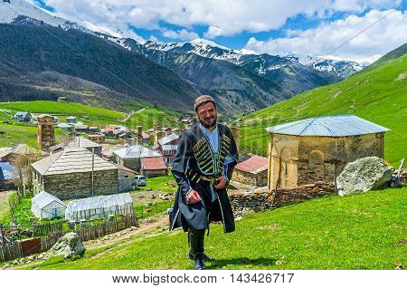 USHGULI GEORGIA - MAY 22 2016: The young Svan in traditional costume poses with the village on the background on May 22 in Ushguli.