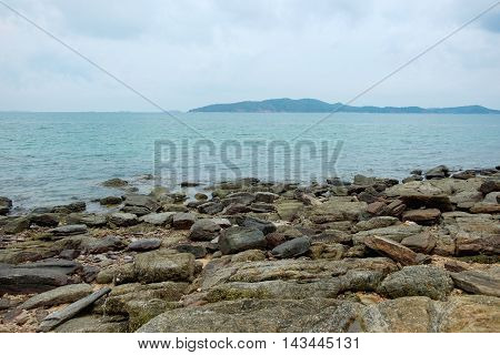 Rocks on shoreline with sea and mountain background at Khao Laem Ya Mu Ko Samet National Park in Thailand.