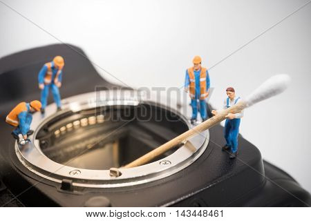 Camera sensor cleaning team . Miniature people working.