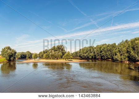 Small idyllic island in a Dutch nature reserve in the summer season. It's a windless day and the contrails remain long visible in the blue sky.