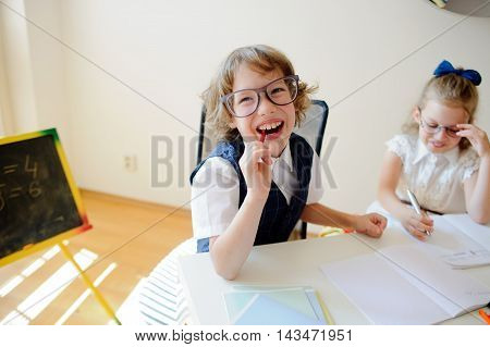 Funny little schoolchildren in glasses boy and girl sit at one desk. It's elementary school students. Children laugh. The deskmate in children are school supplies and textbooks. Back to school.