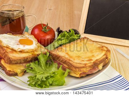 Breakfast and chalkboard  on wooden table
Quick snack with ham and cheese sandwiches cup of tea tomato and fresh salad. Beside the plate with food is a blackboard and chalk for writing messages.