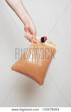 hand holding plastic bag with tap full of apple juice, stucco wall background