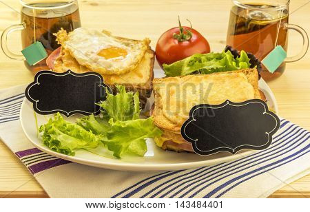 Sandwiches and tea cups for a pair - Plate with sandwiches, fried egg, tomato and green salad on wooden table. Each sandwich has a blank paper tag for short messages.