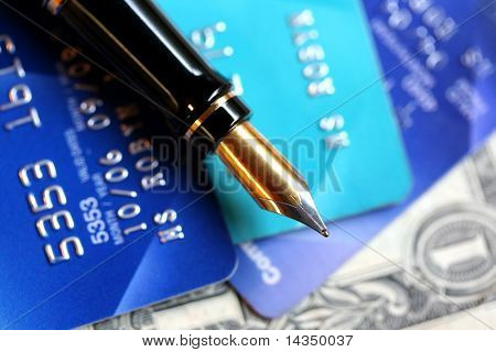 A classic gold-nibbed fountain pen on credit cards and a US one dollar bill.  Focus on nib of pen.