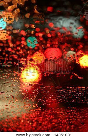 Trafic de nuit pluvieuse ~ lumières dans les gouttes de pluie sur un pare-brise de voiture forment un fond coloré.