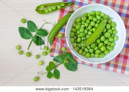 Fresh green peas in white ceramic bowl on wooden background. Top view.