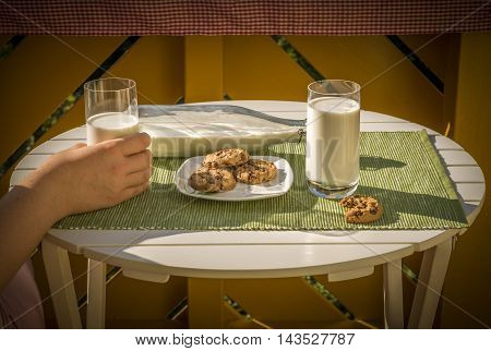 Dessert and milk on table - Glass of milk held in a woman's hand and a plate with cookies, on a white round table, in a warm sunny morning.