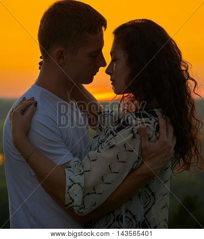 romantic couple embrace at sunset on outdoor, beautiful landscape and bright yellow sky, love tenderness concept, young adult people