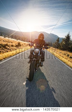 Motorcycle driver riding on motorway in beautiful sunset light. Shot from front view