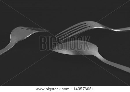 Cutlery set - two forks and a spoon on a black background. Black and white photo