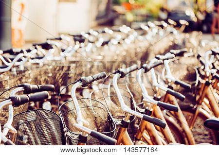 Row Of City Parked Bicycles Bikes For Rent On Sidewalk. Bike Bicycle Parking In European City. Close Up Of Handlebar. Toned Instant Filtered Photo