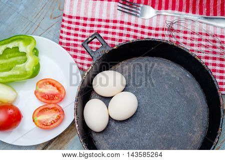 Fresh ingredients for omelet - three eggs in pot vegetables and spices on the wooden rustic table