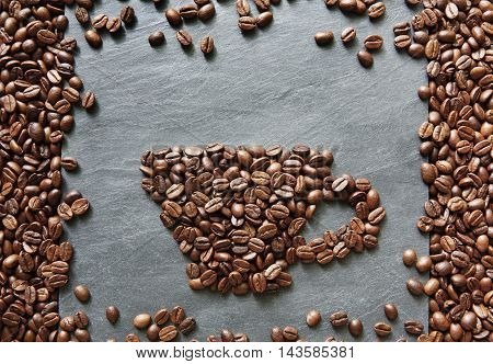 Cup from coffee beans. Heap of roasted coffee bean on grey stone surface texture. Coffee shop or cafe background. Natural stone and cup from beans. Soft color toning, top view
