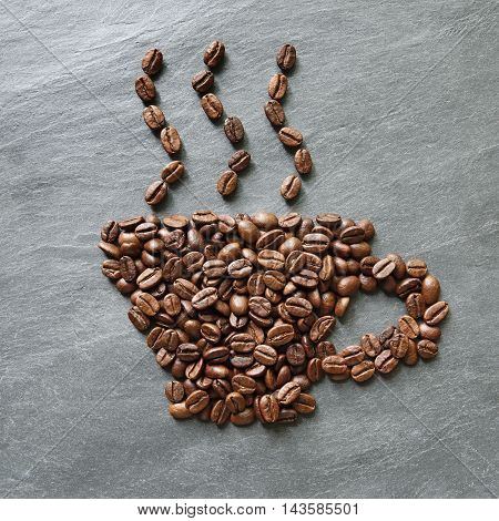 Cup from coffee beans with smoke. Heap of roasted coffee bean on grey stone surface texture. Coffee shop or cafe background. Natural stone and cup from beans. Soft color toning, top view