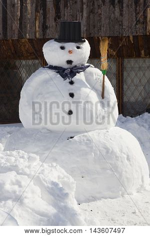 big snowman with broom and hat near fence