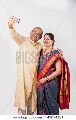 technology and people concept - indian senior couple taking selfie with mobile camera, isolated over white background